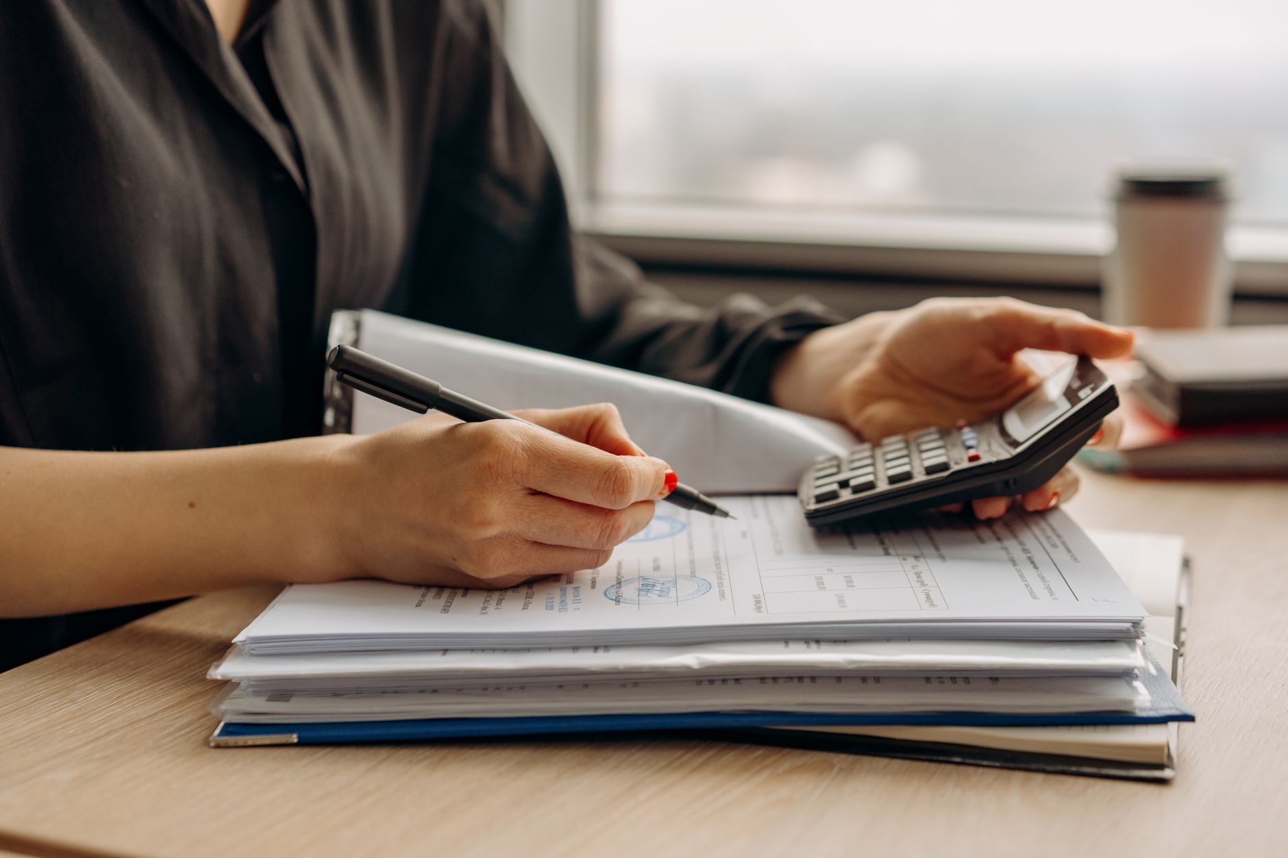 Hands reviewing paperwork and invoices with a calculator, representing checking NDIS claims before submission