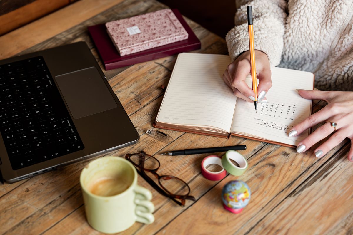 Person writing goals in a notebook with a cup of coffee on a wooden table