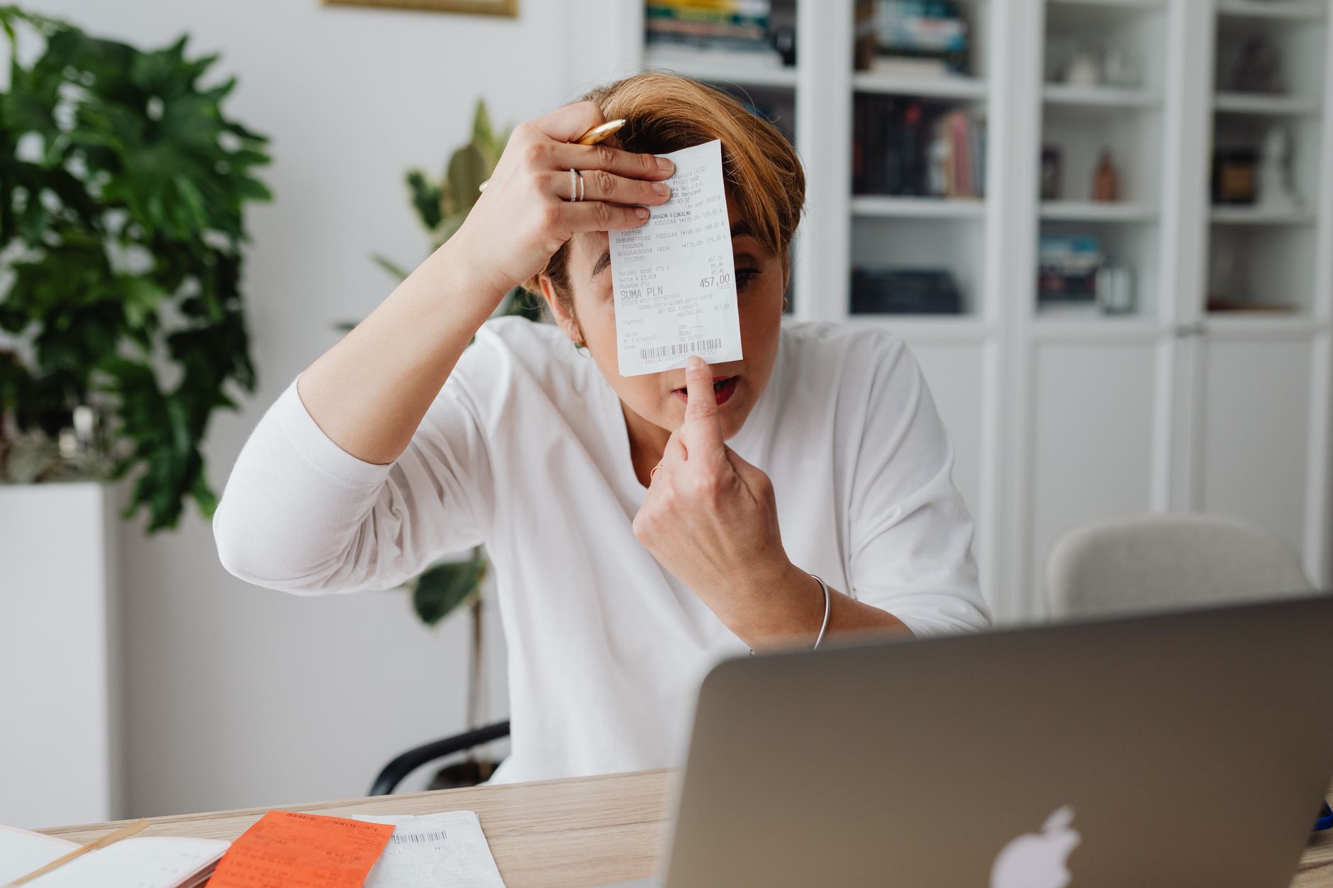 A woman sitting at a desk examining a receipt with concern, cross-referencing it against her laptop — a familiar moment for anyone checking NDIS charges