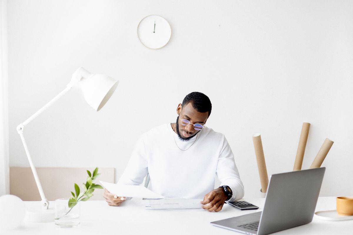 A person sitting at a kitchen table with a laptop, phone, and NDIS paperwork spread out, managing their plan independently