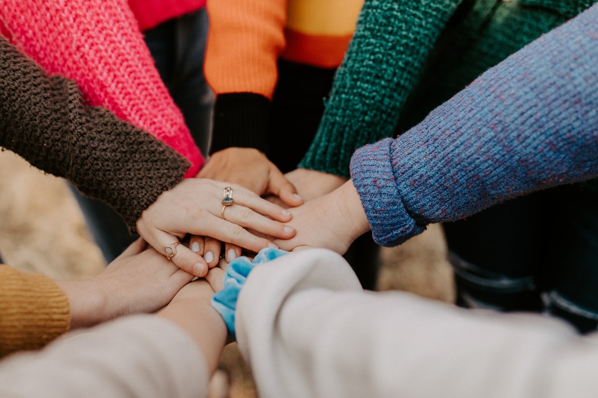 A group of people placing their hands together in a circle, symbolising trust, teamwork, and NDIS support